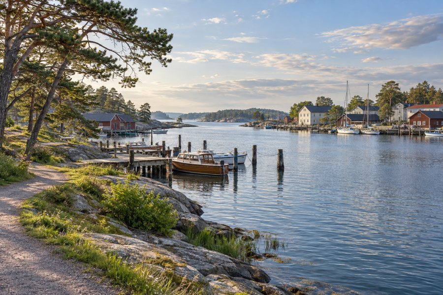 Fiktischer finnischer Küstenhafen mit Booten, grüner Uferpromenade und bewaldeten Inseln